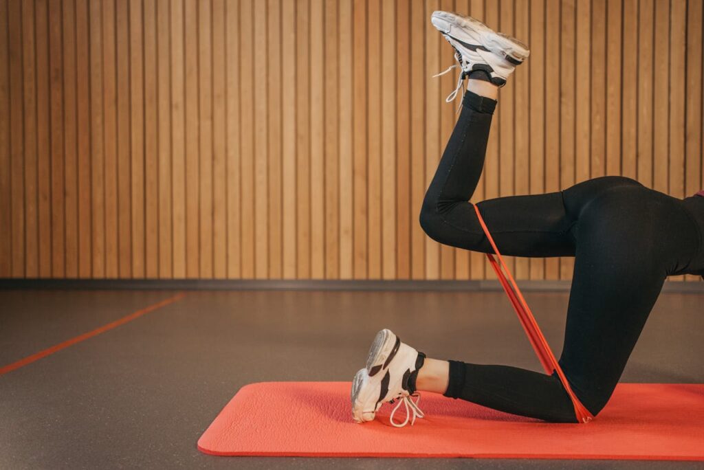 Woman in activewear working out indoors with resistance band on yoga mat, focusing on legs.